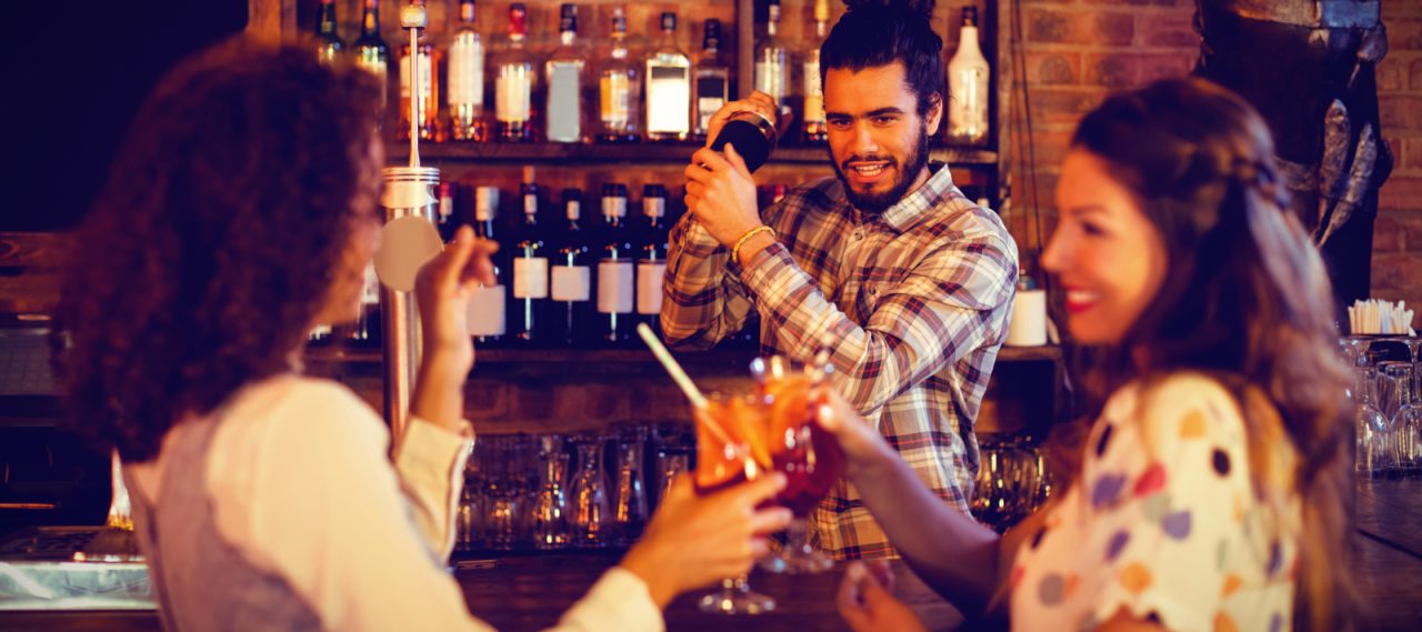 barman avec un shaker à cocktail devant deux femmes